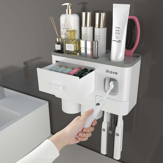 Wall-mounted toothbrush holder and toothpaste dispenser with storage drawer and cups for bathroom organization.