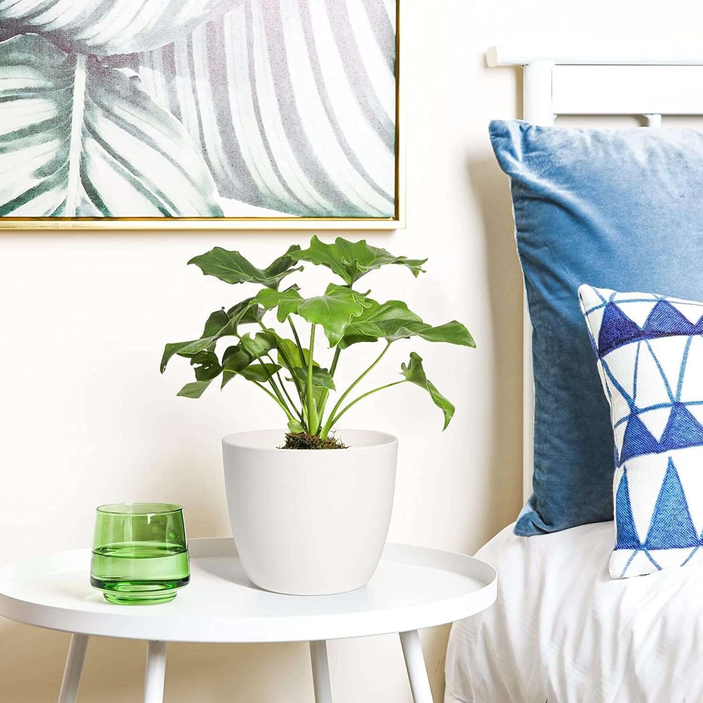 Modern bedroom decor with self-watering planter, houseplant, green glass, and geometric cushions on a white side table.